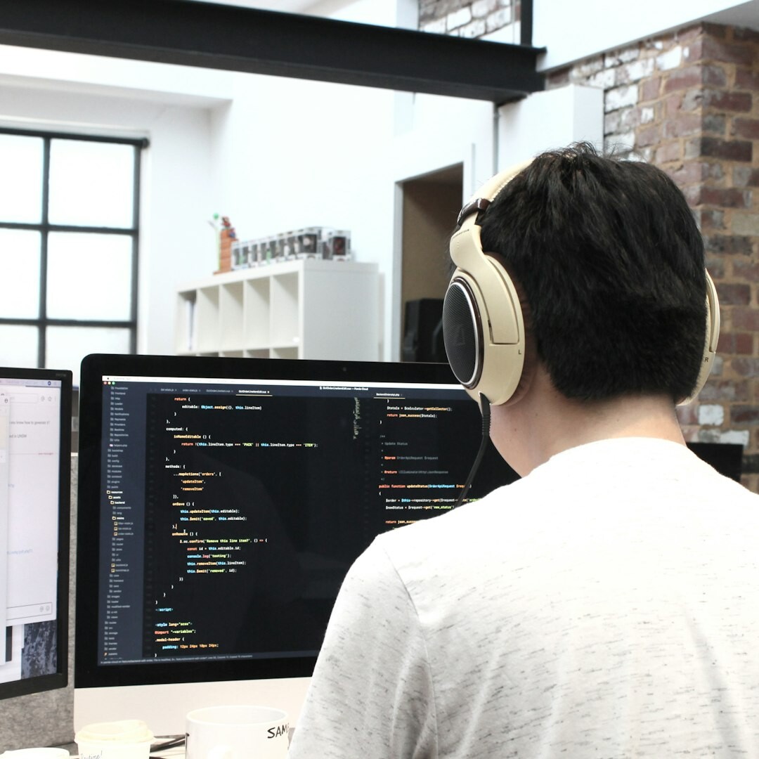 Young Portuguese man coding on a laptop at a desk with two monitors